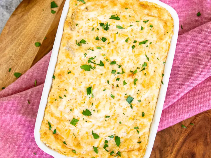 a baking dish with baked maryland crab dip and diced parsley on top of a red napkin and wooden cutting board