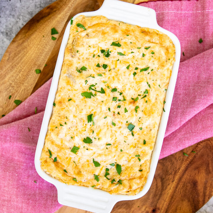 a baking dish with baked maryland crab dip and diced parsley on top of a red napkin and wooden cutting board