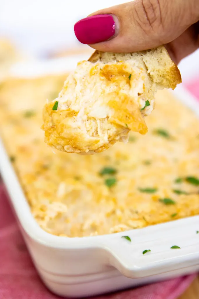 a slice of baguette dipped in crab dip being held up