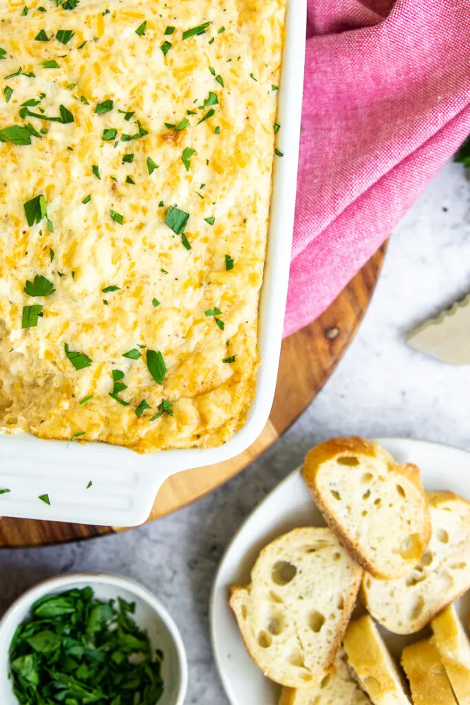 a plate of sliced baguette, a bowl of diced parsley, and maryland crab dip on a red napkin