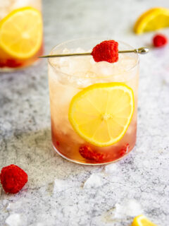 a raspberry bramble surrounded by crushed ice, raspberries, and lemon slices