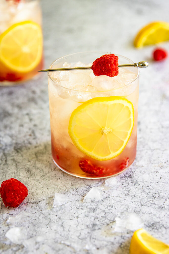 a raspberry bramble surrounded by crushed ice, raspberries, and lemon slices