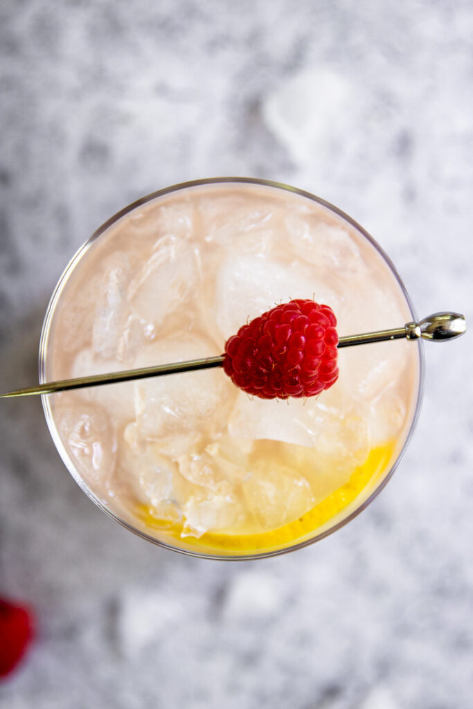 a close up of the top of the cocktail showing crushed ice and a raspberry on a metal pick