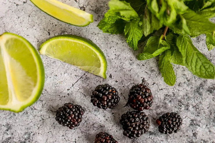 a bunch of mint leaves, lime slices, and fresh blackberries