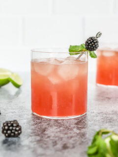 a blackberry bourbon smash in a rocks glass with mint leaves and blackberry on a metal cocktail pick and mint and blackberries scattered