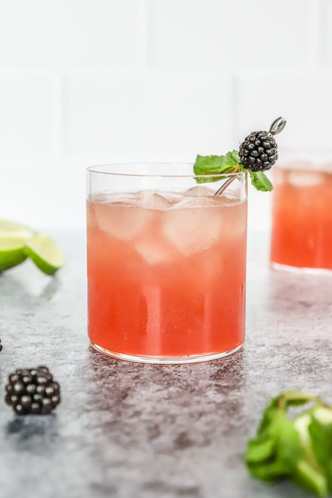 a blackberry bourbon smash in a rocks glass with mint leaves and blackberry on a metal cocktail pick and mint and blackberries scattered