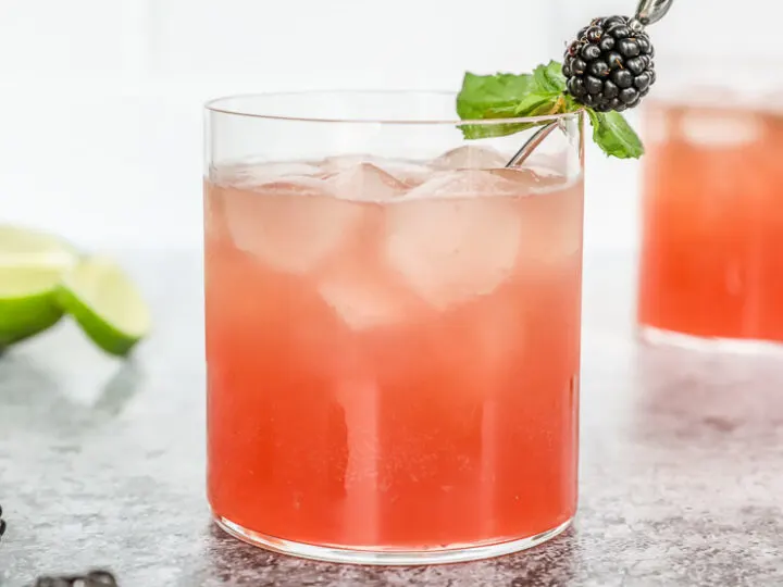 a blackberry bourbon smash in a rocks glass with mint leaves and blackberry on a metal cocktail pick and mint and blackberries scattered