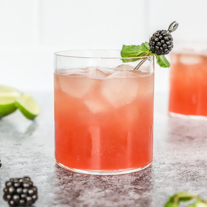 a blackberry bourbon smash in a rocks glass with mint leaves and blackberry on a metal cocktail pick and mint and blackberries scattered