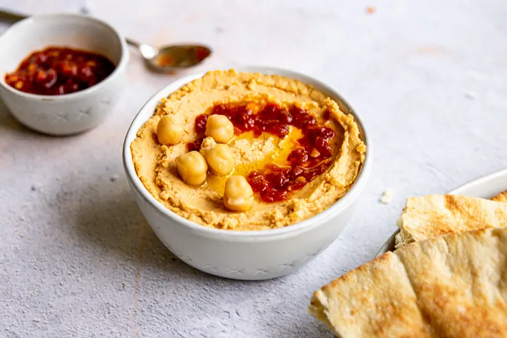 a small bowl of hummus with chickpeas and sambal oelek on top