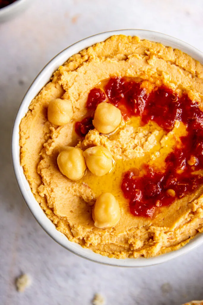 a close up of sambal oelek and chickpeas on a bowl of hummus