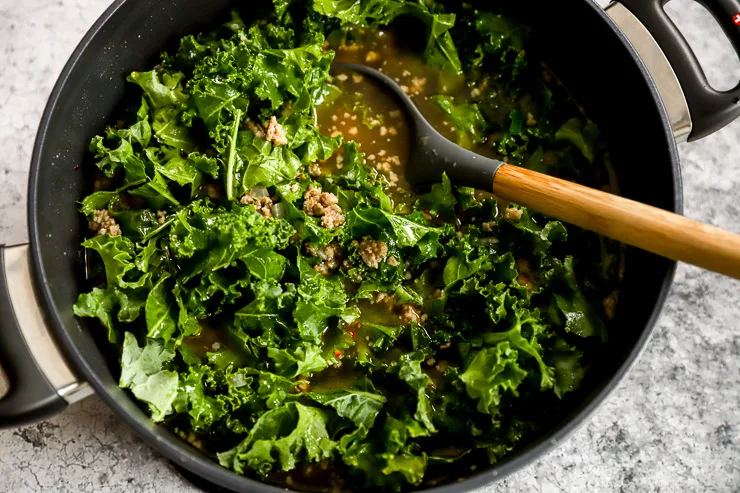 a soup pot with broth, cooked sausage, and chopped kale