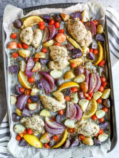 a sheet pan with parchment paper with marinade covered chicken thighs, potatoes, and vegetables