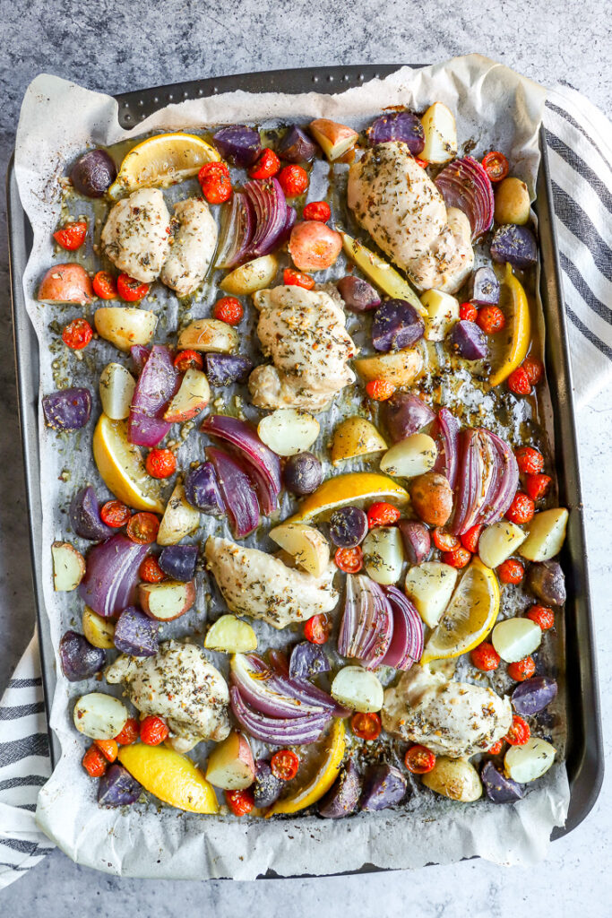 a sheet pan with parchment paper with marinade covered chicken thighs, potatoes, and vegetables