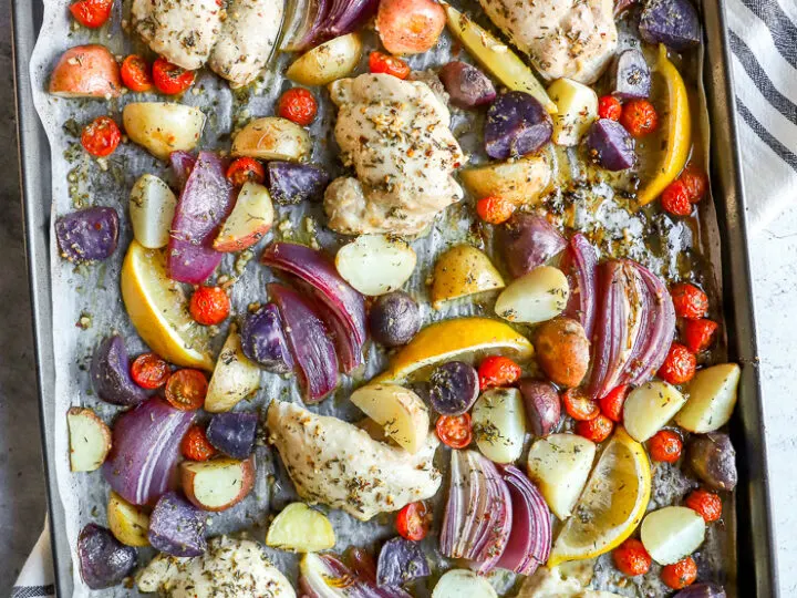 a sheet pan with parchment paper with marinade covered chicken thighs, potatoes, and vegetables