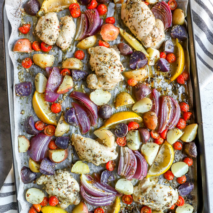 a sheet pan with parchment paper with marinade covered chicken thighs, potatoes, and vegetables