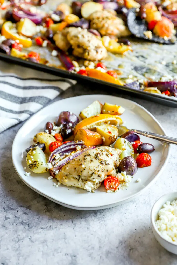 a plate of chicken thighs, potatoes, and veggies next to the sheet pan