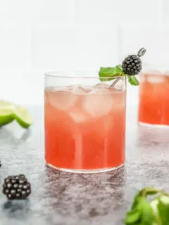 a blackberry bourbon smash in a rocks glass with mint leaves and blackberry on a metal cocktail pick and mint and blackberries scattered