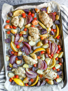 a sheet pan with parchment paper with marinade covered chicken thighs, potatoes, and vegetables