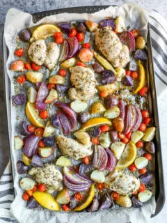 a sheet pan with parchment paper with marinade covered chicken thighs, potatoes, and vegetables