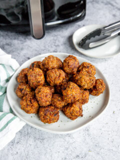 a white plate of air fryer turkey meatballs in front of an air fryer and tongs