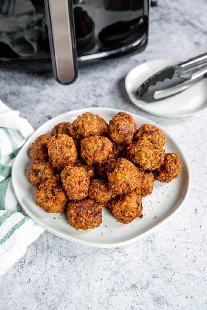 a white plate of air fryer turkey meatballs in front of an air fryer and tongs