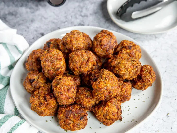 a white plate of air fryer turkey meatballs in front of an air fryer and tongs