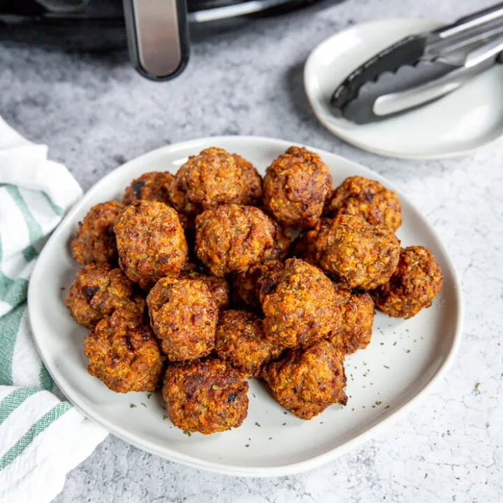 a white plate of air fryer turkey meatballs in front of an air fryer and tongs