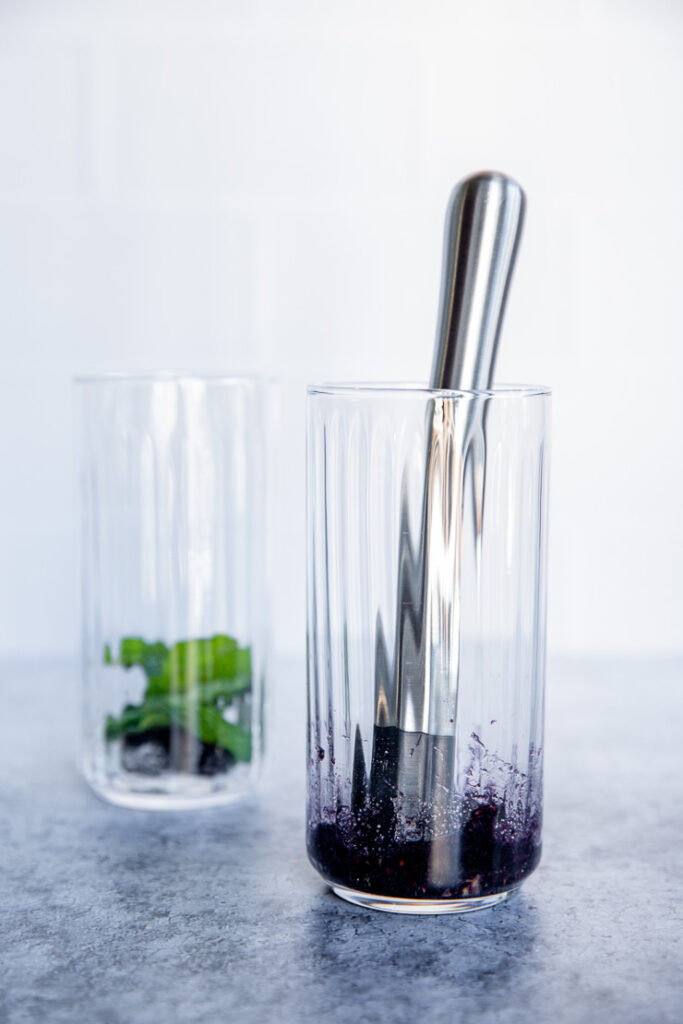 a glass with a muddler and blackberries and mint