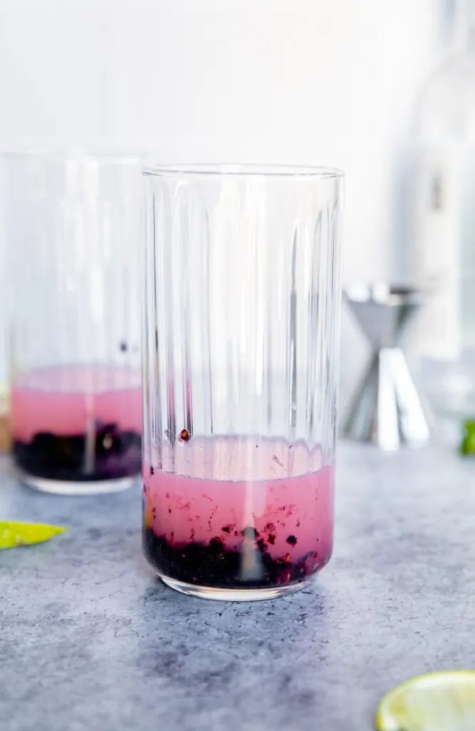 a highball glass with muddled blackberries, mint, and lime juice