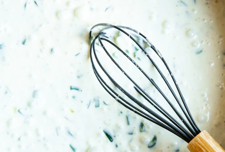 a whisk in a runny cheese mixture with poblano peppers