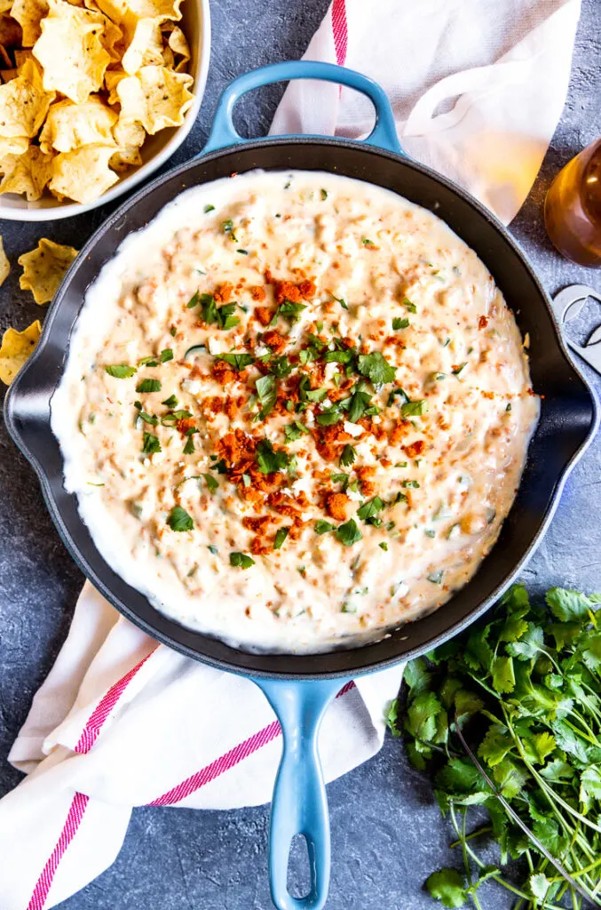 a blue pan with chorizo cheese dip topped with crumbled chorizo and diced cilantro surrounded by tortilla chips and cilantro