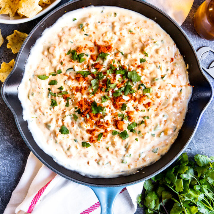 a blue pan with chorizo cheese dip topped with crumbled chorizo and diced cilantro surrounded by tortilla chips and cilantro