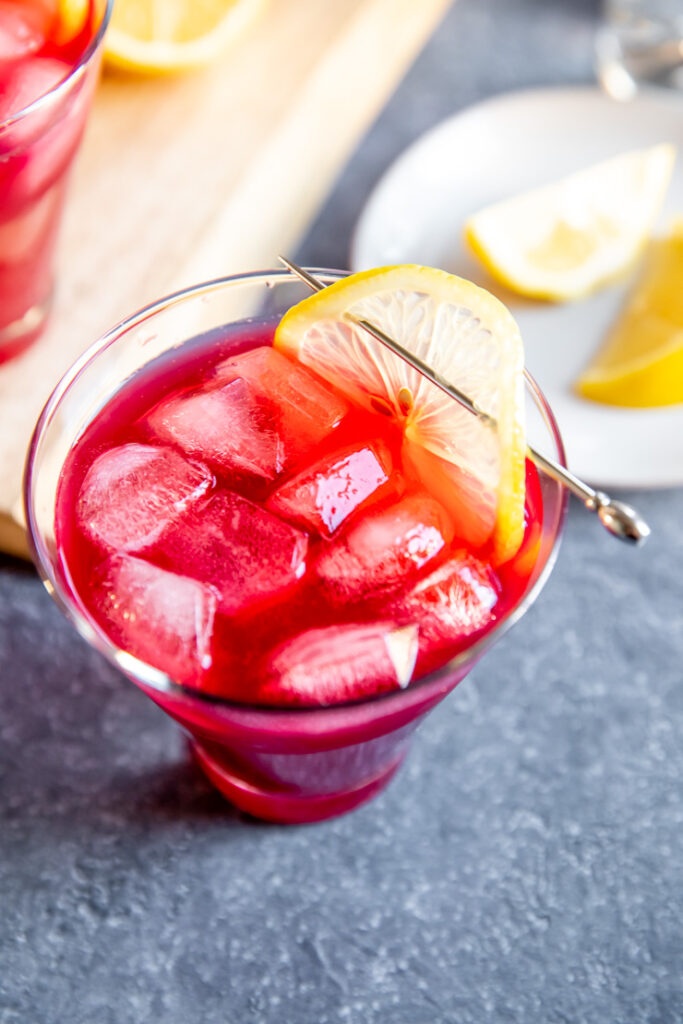 a close up shot of a thin lemon slice on a metal cocktail pick on the maroon cocktail