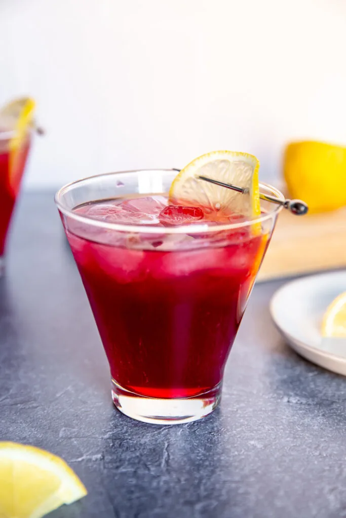 a cosmopolitan glass with cranberry bourbon cocktail and a lemon slice on a cocktail pick