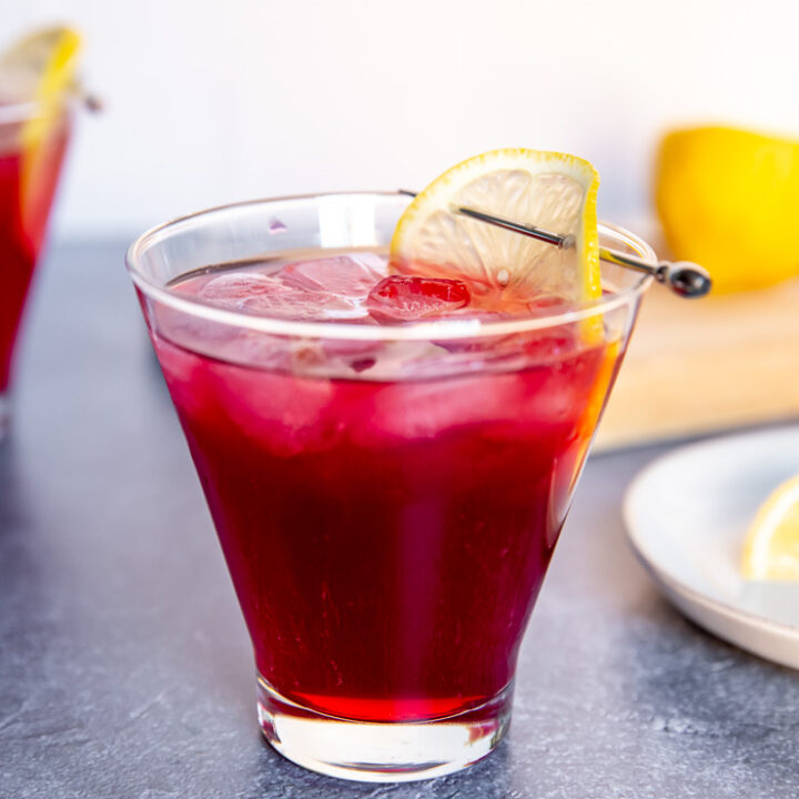 a cosmopolitan glass with cranberry bourbon cocktail and a lemon slice on a cocktail pick