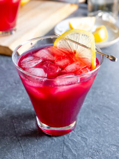 a cosmopolitan glass with cranberry bourbon cocktail and a lemon slice on a cocktail pick on a dark grey background