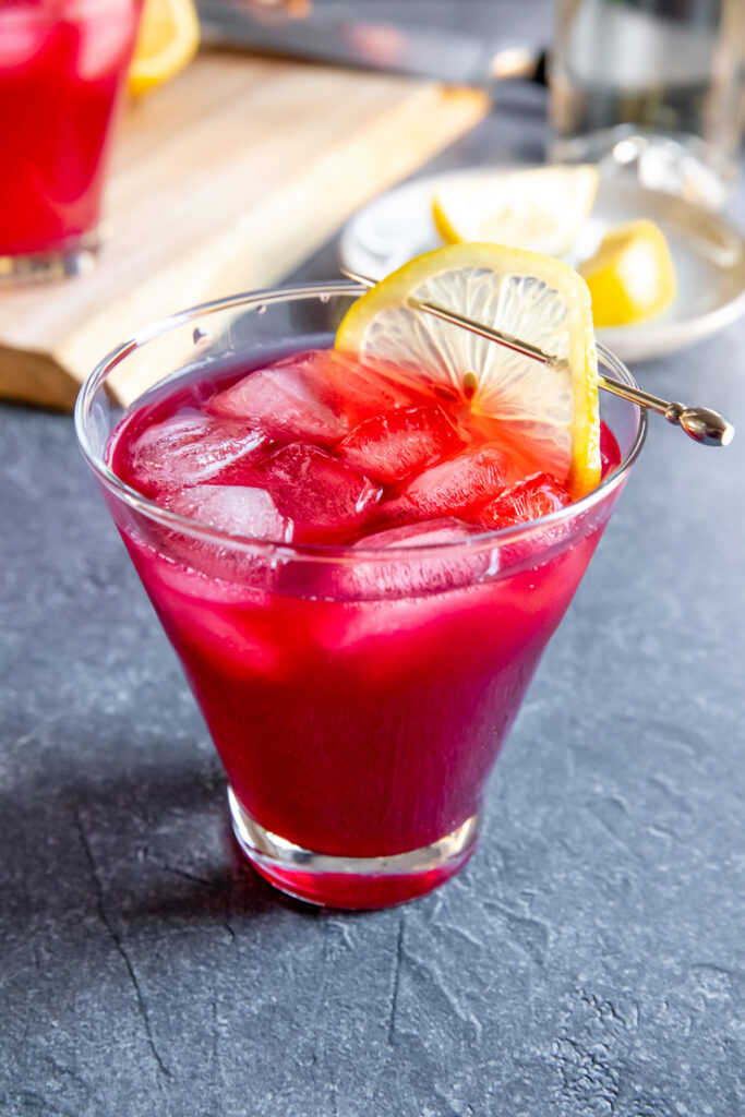 a cosmopolitan glass with cranberry bourbon cocktail and a lemon slice on a cocktail pick on a dark grey background