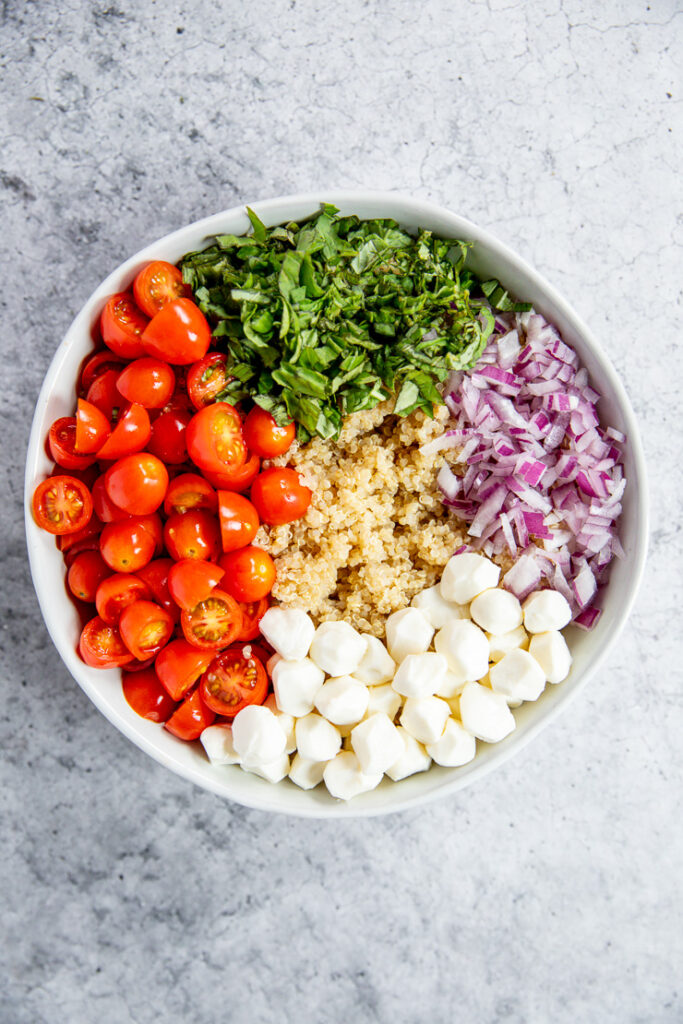 halved grape tomatoes, diced basil, diced red onion, pearl mozzarella, and quinoa grouped together in a bowl