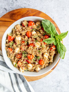 a bowl of italian quinoa salad on a wood cutting board with a napkin and basil garnish