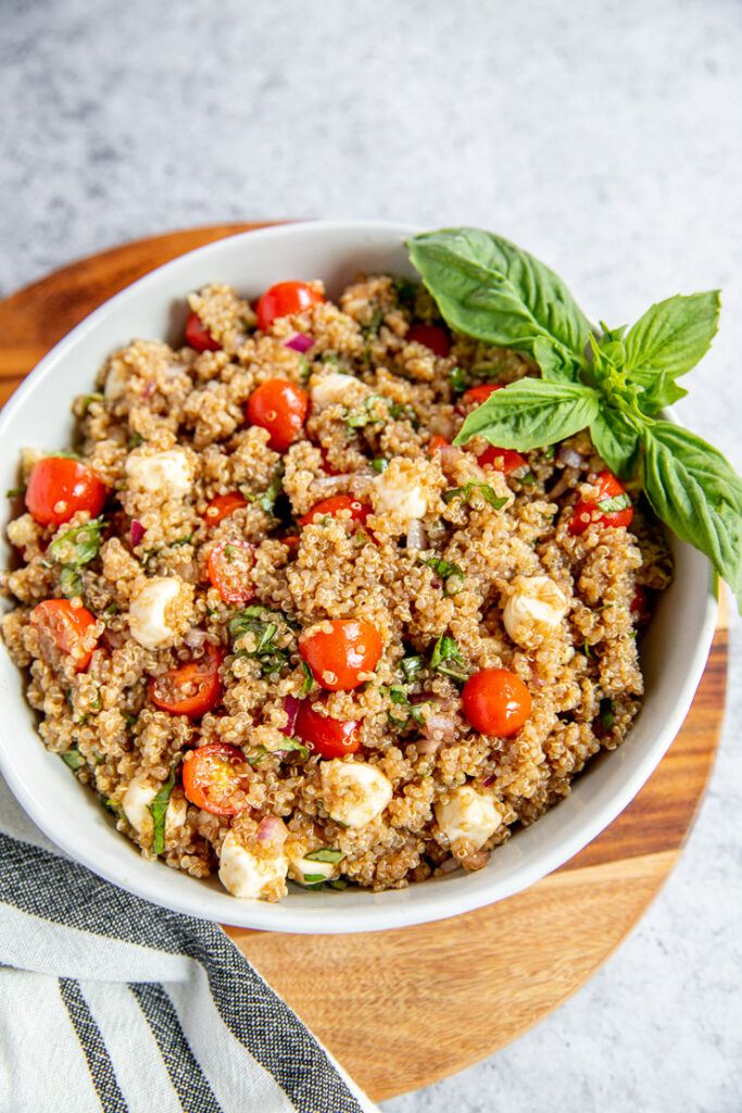 a white bowl full of italian quinoa salad and a basil garnish