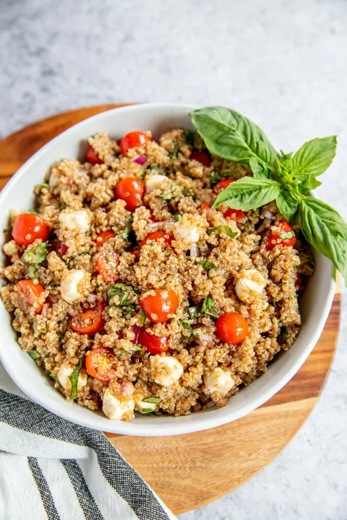 a white bowl full of italian quinoa salad and a basil garnish