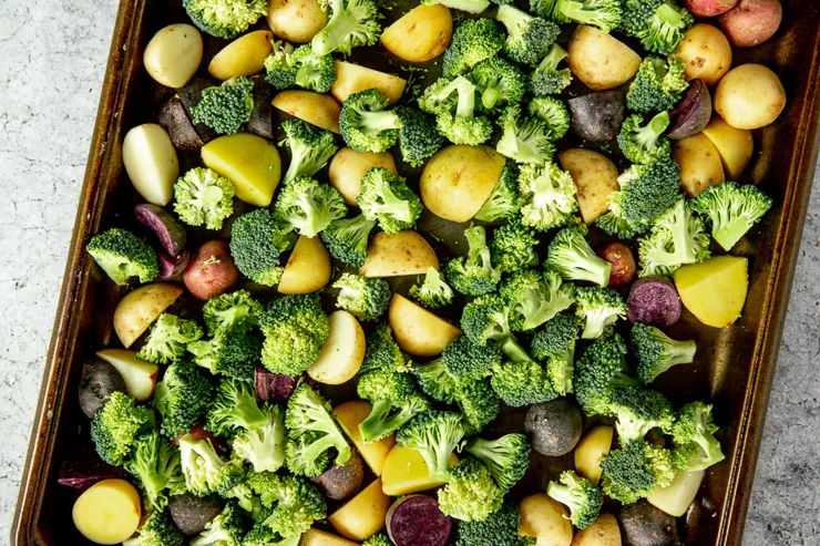 a sheet pan with raw broccoli florets and quartered tri color potatoes