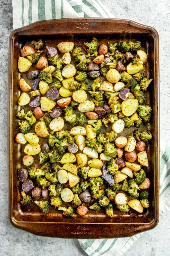 a sheet pan of roasted potatoes and broccoli on a white and green striped napkin