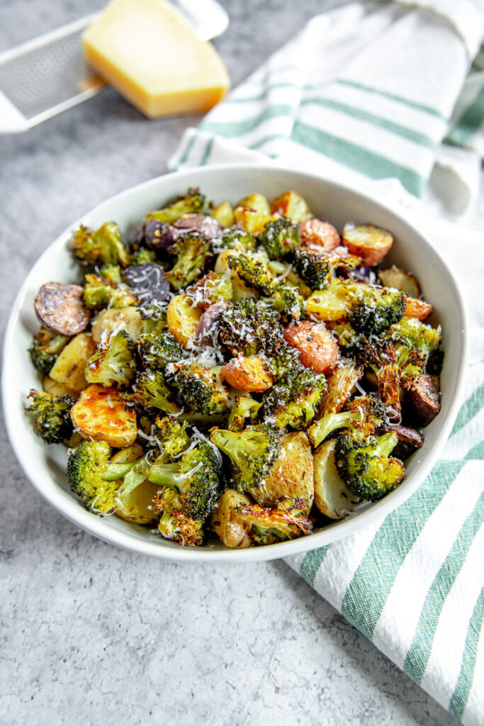 a close up of shaved parmesan on roasted potatoes and broccoli in a bowl