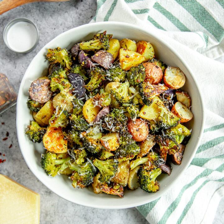 an overhead shot of a bowl of roasted potatoes and broccoli next to a white and green napkin and parmesan grater