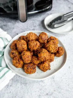 a white plate of air fryer turkey meatballs in front of an air fryer and tongs