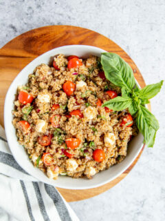 a bowl of italian quinoa salad on a wood cutting board with a napkin and basil garnish