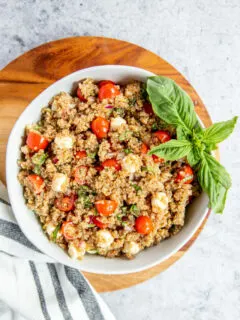 a bowl of italian quinoa salad on a wood cutting board with a napkin and basil garnish