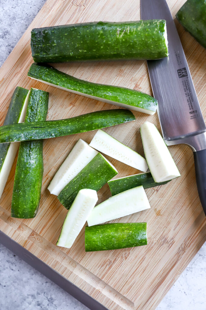 zucchini on a cutting board next to a knife cut into wedges