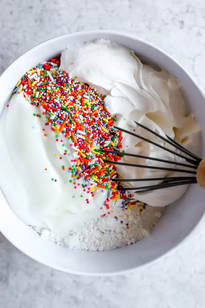 funfetti cake mix, sprinkles, yogurt, and cool whip in a mixing bowl